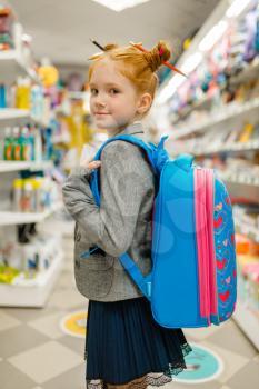 Little school girl with backpack in stationery store. Female child buying office supplies in shop, schoolchild in supermarket