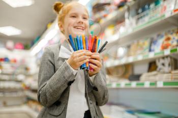Little school girl holds colorful markers, shopping in stationery store. Female child buying office supplies in shop, schoolchild in supermarket
