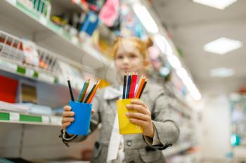 Little schoolgirl holds glasses with pencils, shopping in stationery store. Female child buying office supplies in shop, schoolchildat the shelf in supermarket