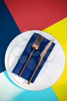 Table setting, silverware on the plate closeup, top view, nobody. Banquet decoration, colorful tablecloth and blue napkin, tableware outdoors