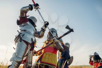 Medieval knights in armor and helmets fight with sword and axe, great battle. Armored ancient warrior in armour posing in the field