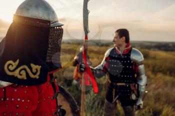 Medieval knights in armor and helmet at sunset, great tournament. Armored ancient warrior in armour posing in the field