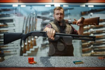 Man with two rifles at counter in gun shop. Euqipment for hunters on stand in weapon store, hunting and sport shooting hobby