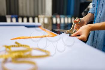 Seamstress cuts fabric with scissors in textile store. Woman works with cloth for sewing, female tailor in workshop