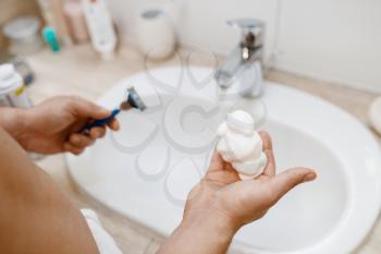Man squeezes out shaving foam on hand in bathroom, routine morning hygiene. Male person at the sink performs skin and body treatment procedures