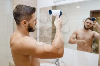 Man dries his hairstyle with a hair dryer, morning hygiene procedures. Athletic male person at the mirror in bathroom