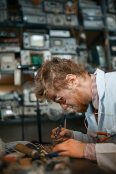 Strange scientist works with soldering iron, test in laboratory. Electrical testing tools on background. Lab equipment, engineering workshop