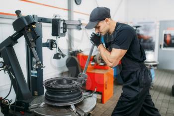 Mechanic fixing broken wheel, tire repairing service. Man repairs car tyre in garage, professional automobile inspection in workshop