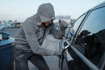 Car thief breaking door lock, criminal job, burglar. Hooded male robber opening vehicle on parking. Auto robbery, automobile crime, vandalism