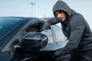 Car thief breaking door, criminal job, burglar, stealing. Hooded male robber opening vehicle on parking. Auto robbery, automobile crime, vandalism