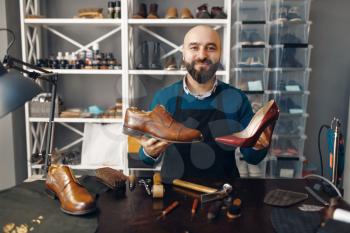 Bootmaker shows repaired shoes, footwear repair service. Craftsman skill, shoemaking workshop, master works with boots, cobbler