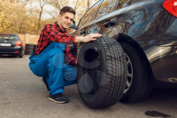Male worker in uniform fixing problem with tire, tyre service. Vehicle repair service or business, man repairing broken wheel