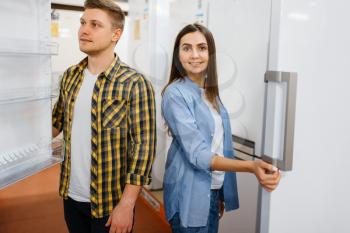 Young family couple choosing refrigerator in electronics store. Man and woman buying home electrical appliances in market