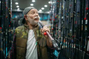 Male angler holds rod in fishing shop. Equipment and tools for fish catching and hunting, accessory choice on showcase in store, spinnings and telescopes assortment