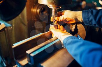 Male technician in uniform and helmet works on lathe, plant. Industrial production, metalwork engineering, machines manufacturing