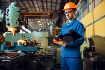Male worker with notebook, lathe on background, plant. Industrial production, metalwork engineering, power machines manufacturing