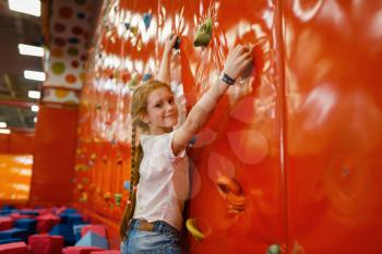 Little girl on climbing wall in the entertainment center. Female child leisures on holidays, childhood happiness, happy kids on playground