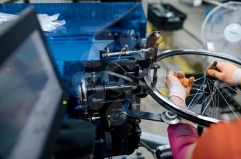 Worker with machine tool installs new bicycle rim on factory, closeup. Bike wheels assembly in workshop, cycle parts installation