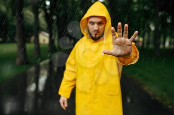 Man in raincoat reach out hand, summer park, rainy day. Alone male person in rain cape on walking path, wet weather in alley