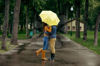 Love couple kissing in park, summer rainy day. Man and woman stand under umbrella in rain, romantic date on walking path, wet weather in alley