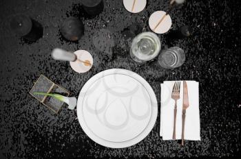 Table setting, glasses, candles and plate on black, top view, nobody. Luxury silverware, tableware outdoors, elegant decoration. Romantic celebration on summer meadow