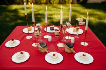 Table setting, tea party with sweets and honey, nobody. Luxury silverware on red tablecloth, tableware outdoors. Wedding celebration on summer meadow