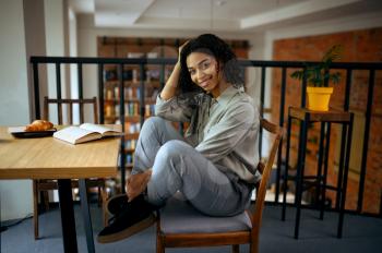 Cheerful female student sitting at the table in library cafe. Woman learning a subject, education and knowledge. Girl studying in campus cafeteria