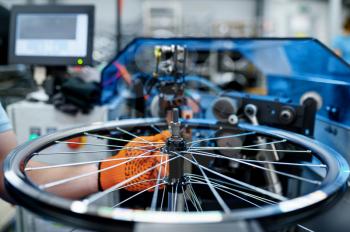 Worker with machine tool checks bicycle rim on backlash, factory. Bike wheels assembly in workshop, cycle parts installation