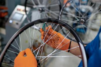 Worker in gloves installs new bicycle spokes on factory. Bike wheels assembly in workshop, cycle parts installation, modern technology