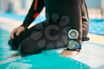 Male diver in scuba gear sitting at the poolside, diving school. Teaching people to swim underwater, indoor swimming pool interior on background