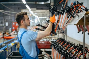 Bicycle factory, worker at bike assembly line. Male mechanic in uniform installs cycle parts in workshop, industrial manufacturing