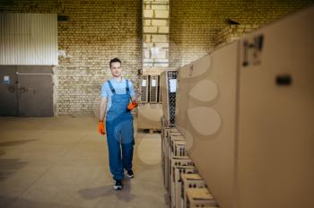 Bicycle factory, worker sits on boxes with bikes. Male mechanic in uniform at the packs with cycle parts, assembly line in workshop, industrial manufacturing