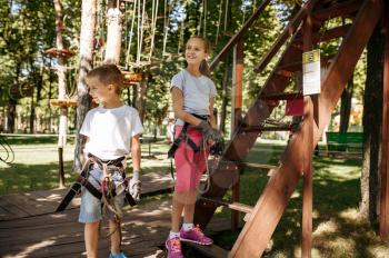 Little kids in equipment, rope park, playground. Children climbing on suspension bridge, extreme sport adventure on vacations, danger entertainment outdoors