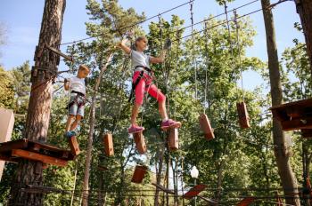 Brave kids in equipment climbs in rope park, playground. Children climbing on suspension bridge, extreme sport adventure on vacations, danger entertainment outdoors