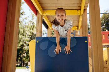 Happy little girl poses on playground, children's town. Child climbing on suspension bridge, extreme sport adventure on vacations, danger entertainment outdoors