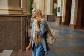 Arab female student with books at university entrance. Muslim woman in hijab holds textbooks outdoors. Religion and education