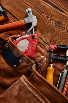 Hammer, stapler and screwdrivers, measuring tape and hacksaw in leather case on wooden background, nobody. Professional instrument, carpenter equipment, fastening, tapping and screwing tools