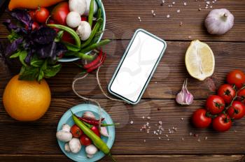 Fresh vegetables in plates and phone on wooden background. Organic vegetarian food, grocery assortment, natural products, healthy lifestyle concept