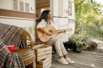 Woman with guitar sitting at the rv entrance, camping in a trailer. Couple travels on van, romantic vacations on motorhome, camper leisures in camping-car, camp