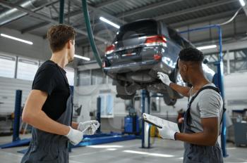 Two male mechanics talking in car service. Vehicle repairing garage, men in uniform, automobile station interior on background. Professional auto diagnostic