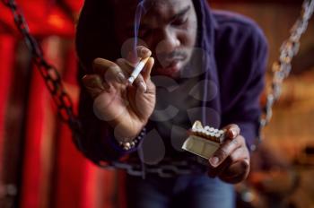 Drug addict man smokes a cigarette in den, junkie in withdrawal. Narcotic addiction problem, eternal depression of junky people