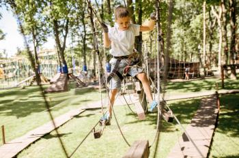Little boy climbs in rope park at sunny day. Child climbing on suspension bridge, extreme sport adventure on vacations, entertainment outdoors