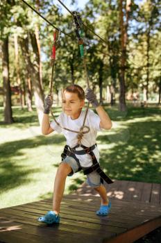 Little boy climbs in rope park, top view climber on playground. Child climbing on suspension bridge, extreme sport adventure on vacations, entertainment outdoors