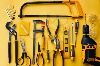 Professional workshop instrument, top view, yellow background, nobody. Carpenter tools, builder equipment, screwdriver and piles, hacksaw and level, scissors and drill