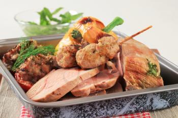 Roast pork, stuffed pepper and tomatoes and kebabs in a baking pan