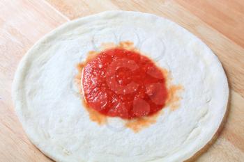 Tomato paste spread on raw pizza dough 