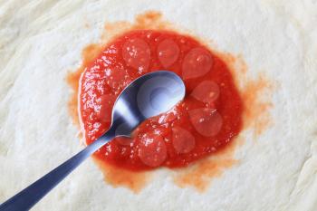 Tomato paste spread on raw pizza dough 