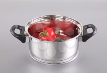 Red tomato in a shiny stainless steel pot 