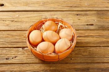 Fresh brown eggs in terracotta bowl on wooden table
