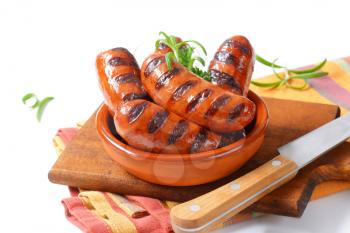 bowl of grilled sausages with parsley and rosemary on wooden cutting board